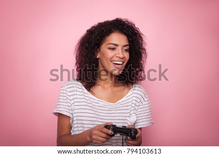 Young african woman play with joystick on pink background