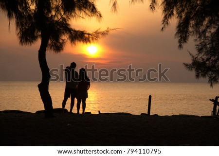 One couple is loving each other and taking pictures together with the bright orange sunset in the morning, rising from the sea at one of the beaches.