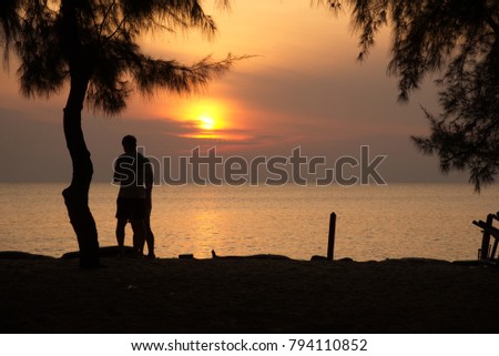 One couple is loving each other and taking pictures together with the bright orange sunset in the morning, rising from the sea at one of the beaches.