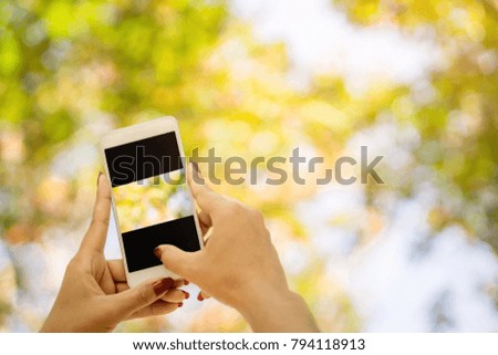 woman hand holding smart phone outdoor  taking photo of colorful nature forest during traveling in autumn season, abstract nature bokeh background