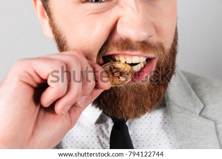 Close up portrait of a man biting golden bitcoin isolated over gray background Royalty-Free Stock Photo #794122744