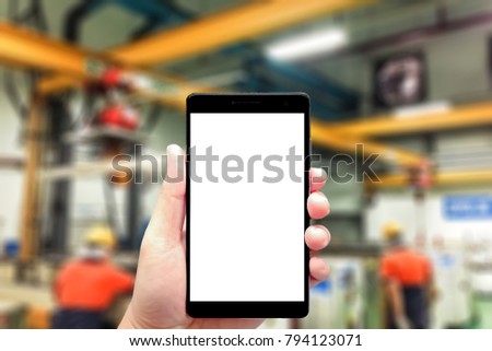 left hand using smartphone with blank screen on Abstract blurred background of operator working in heavy manufacturing factory
