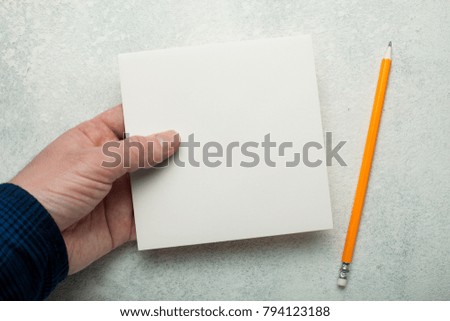 An empty square piece of paper in a man's hand, a yellow pencil next to it. Mock-up.