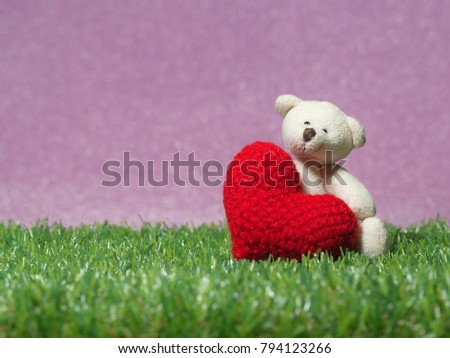Teddy bear holding a handmade red heart on green grass background is royal pink.Copy space for text, Valentines day, love concept and love background