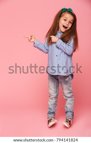 Full-length picture of funny little girl gesturing pointing index finger isolated over pink background, copy space for your text or product