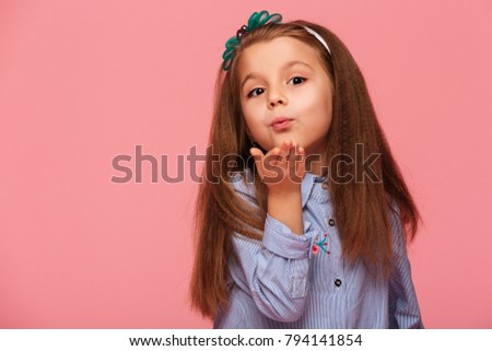 Portrait of adorable little girl 5-6 years with beautiful long auburn hair, blowing air kiss on camera over pink background