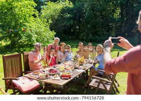 leisure, holidays and people concept - happy family having festive dinner or summer garden party and photographing by smartphone