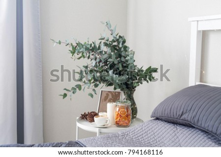 Eucalyptus in the interior, morning coffee on the table in the bedroom by the bed. Decorative orange chips, cones, candles, cappuccino