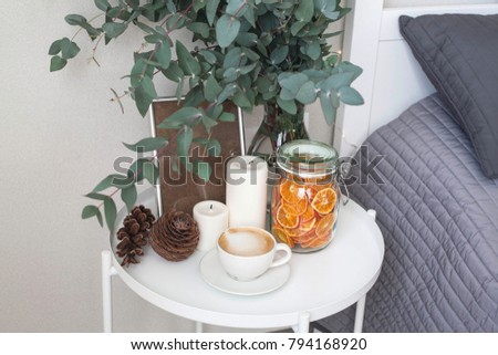 Eucalyptus in the interior, morning coffee on the table in the bedroom by the bed. Decorative orange chips, cones, candles, cappuccino