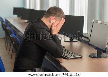 tired man in a black shirt asleep at his desk on a background of LCD monitors