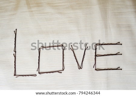 Write a love written by hairpins-ignoramuses on a beige background. The word love is made up of female ornaments.
