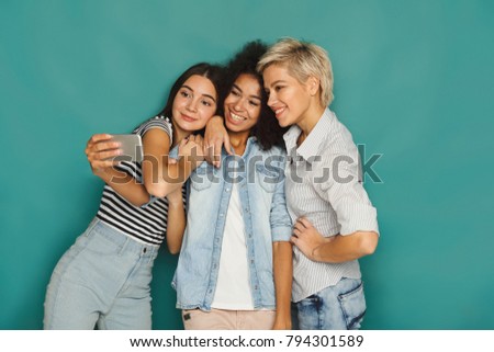 Three happy smiling women taking selfie at blue studio background, copy space