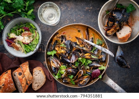 Traditional French blue mussel in bouillabaisse with lettuce and baguette as top view in a casserole 