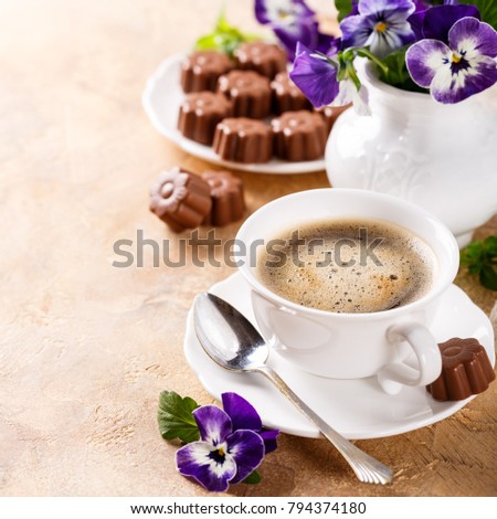 Postcard with cup of cooffee, chocolate candies in flower shape and violets. Holiday food concept with copy space.