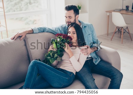 You are my everything, the biggest treasure! Beautiful careless relaxed peaceful wearing casual clothes two people in love sitting cuddling, hugging, embracing on a sofa with closed eyes with flowers