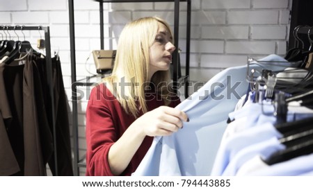Blonde woman wearing a red sweater is choosing clothes for office in a store. Handheld real time medium shot