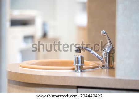 Side perspective close up on a metal faucet with a soap dispenser and beige sink, in a dental office
