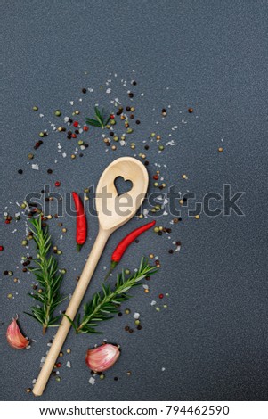 Kitchen wooden spoon with heart frame, pepper, peperoni, salt, rosemary, garlic, on dark grey kitchen counter top  background, top view. Herbs and spices cooking top table.