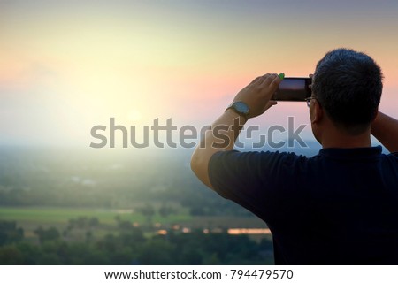 Man taking a photo of a sunset with a phone
