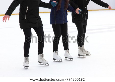 three girls holding hands ice-skating on the ice rink
