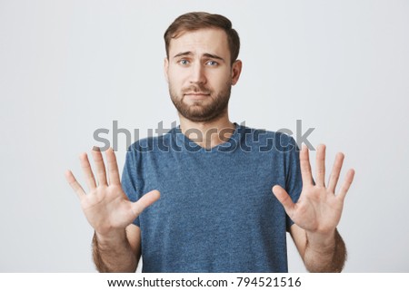 Body language. Disgusted stressed out angry bearded man in blue t-shirt posing against studio wall, keeping hands in stop gesture, trying to defend himself as if saying: Stay away from me Royalty-Free Stock Photo #794521516