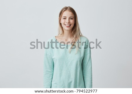 Horizontal portrait of pleasant-looking Caucasian female with long blonde hair, wearing white casual blue sweater, looking happily at camera. Beauty and youth Royalty-Free Stock Photo #794522977