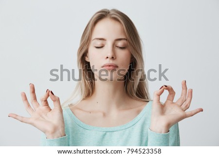 People, yoga and healthy lifestyle. Gorgeous young blonde woman dressed in light blue sweater keeping eyes closed while meditating indoors, practicing peace of mind, keeping fingers in mudra gesture Royalty-Free Stock Photo #794523358