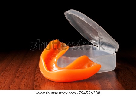Orange mouthguard near opened case on the wooden texture and black background Royalty-Free Stock Photo #794526388