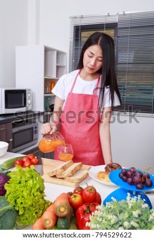 housewife with pouring orange juice jar in kitchen room at home