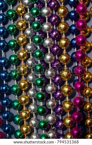 Close up image of Mardi Gras beads hanging on neutral color board background