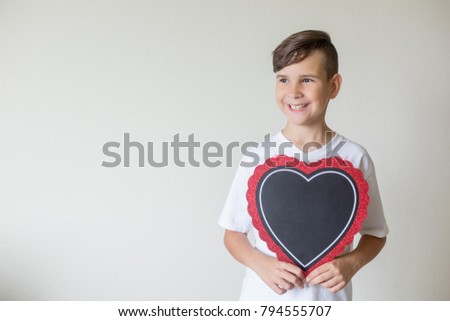 The boy holds a chalkboard in the form of a heart in his hands. Free space for text. Beautiful smile. Portrait. Valentine's Day, Mother's Day, International Women's Day. Father and son. Father's day