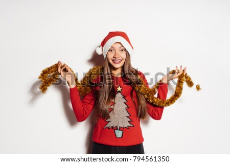 happy young girl in a red cap like Santa Claus holding a golden tinsel, waiting for the new year