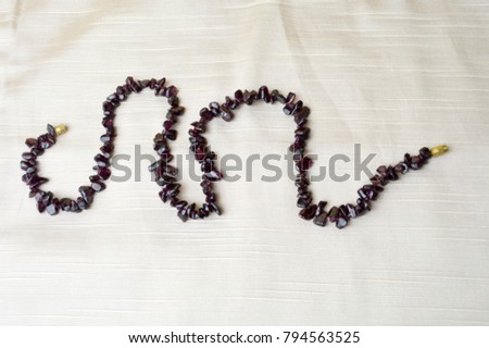 Women's beautiful beads, a necklace of brown dark stones, amber arranged by a snake, a wave against a background of beige cloth and a place for text.