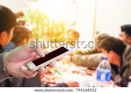 Man use mobile phone, blur images of party between friends as background.