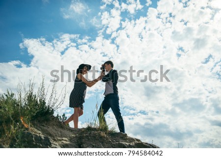 young couple on the hill, man taking picture of his girlfriend that posing in dress