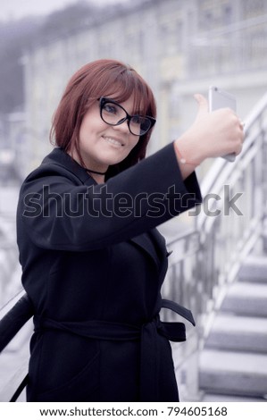 Beautiful girl making selfie in the city. She is smiling and happy.  Making selfie. Close up of the girl with a phone in her hand. Fashion photography. 
