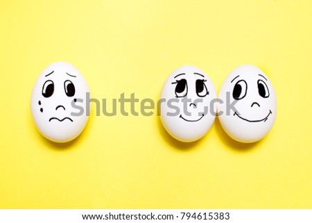 Three eggs with drawn cartoon faces on yellow background. Jealousy concept