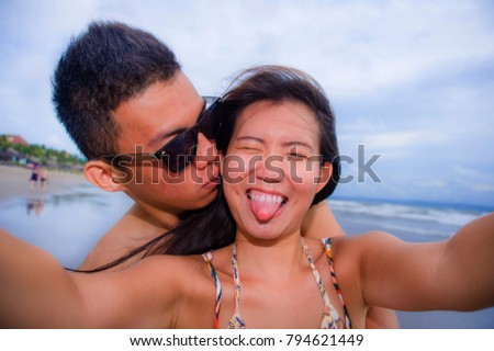 young happy and beautiful Asian Chinese couple taking selfie photo with mobile phone camera smiling joyful having fun on the beach in romance and lovers holidays trip picture concept