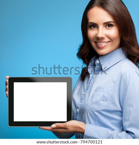 Happy smiling attractive young businesswoman showing blank no-name tablet pc monitor, on blue background, with copyspace area