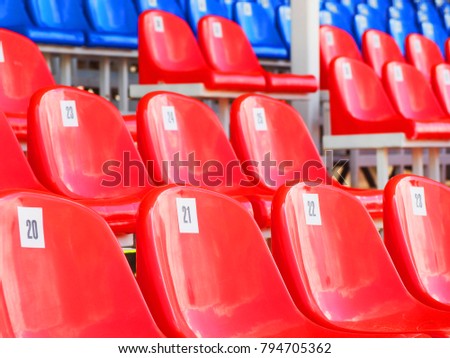 Tribune of stadium. Red and blue numbered empty plastic armchairs. Seats for spectators stand in a row. Passage between tribunes