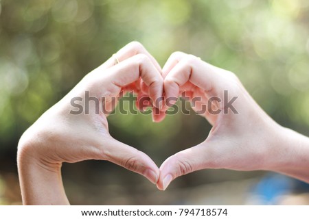 Close-up of Hands in shape of love heart on nature green bokeh sun light and blurred leaf abstract background. 
Vintage tone color.  Valentine concept