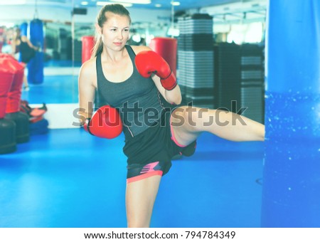 Cheerful positive smiling woman boxer is training kick in box gym.