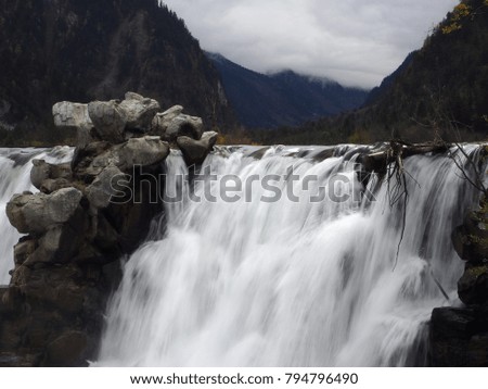Waterfall and stream in the park with high mountain background. Travel, tourism, holidays, nature concept.
