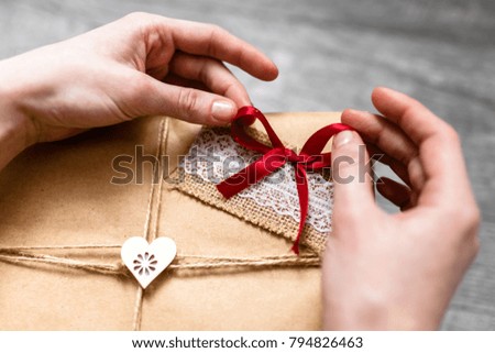 Female hand holding a wrapped gift ,Valentine's Day, romantic photo . Romantic grey wooden background with hearts and gifts, suitable for advertising stylish photo