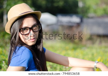 Happy Asian female in cowgirl hat and wear glasses,Sitting on meadow and looking at camera with toothy smile