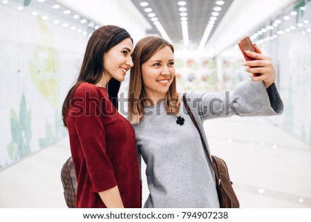 Two young girlfriends stopped doing selfie on phone looking at camera