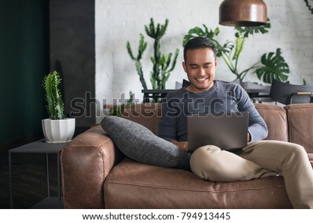 Young happy Asian man using the laptop at home. Royalty-Free Stock Photo #794913445