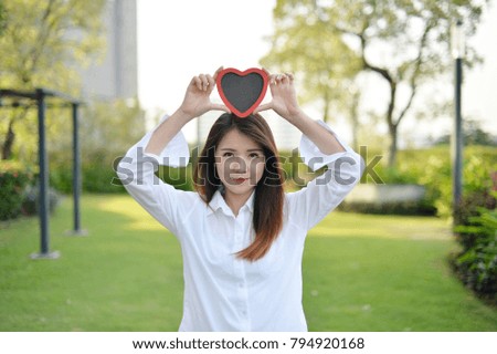 Beautiful asian woman smiling cute  holding red heart for love valentines with garden background.