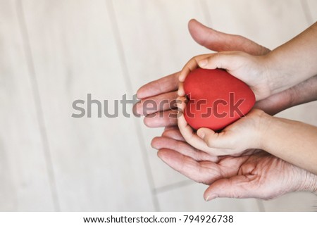 Red heart in child kid and grandmother hands on the grey background