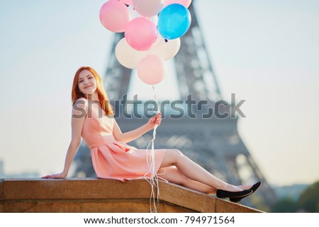 Happy young girl with bunch of pink and blue balloons in front of the Eiffel tower in Paris, France